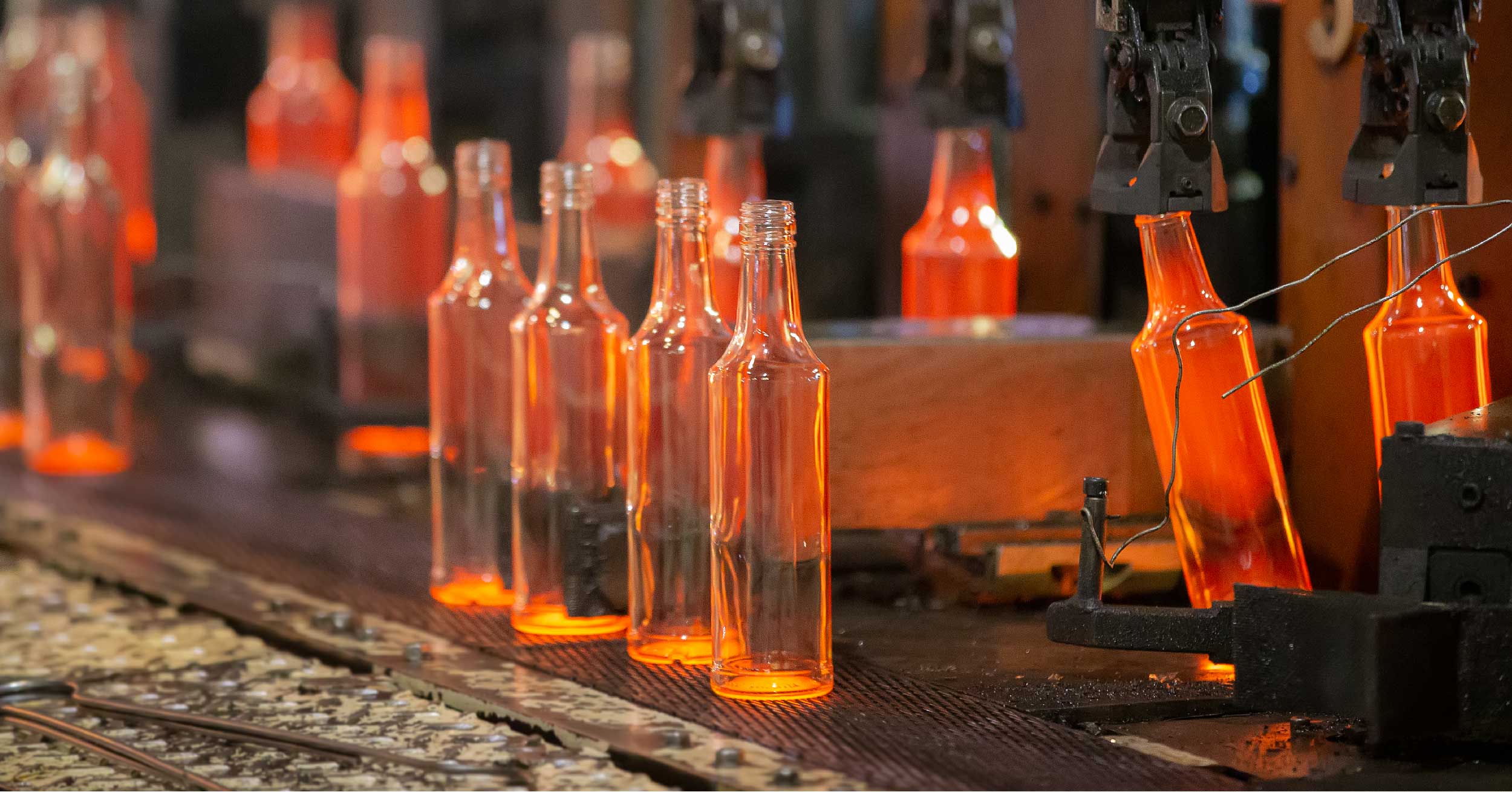 Red hot glass bottles in a glass manufacturing plant with a conveyor belt. Glass manufacturing is a critical process and it is very sensitive to poor power quality issues like harmonic distortion.